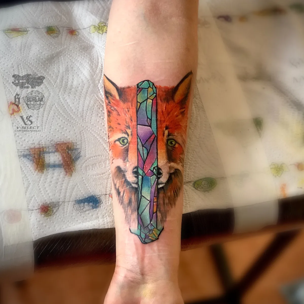 A tattoo of a realistic fox face split down the centre by a colourful geometric crystal design.