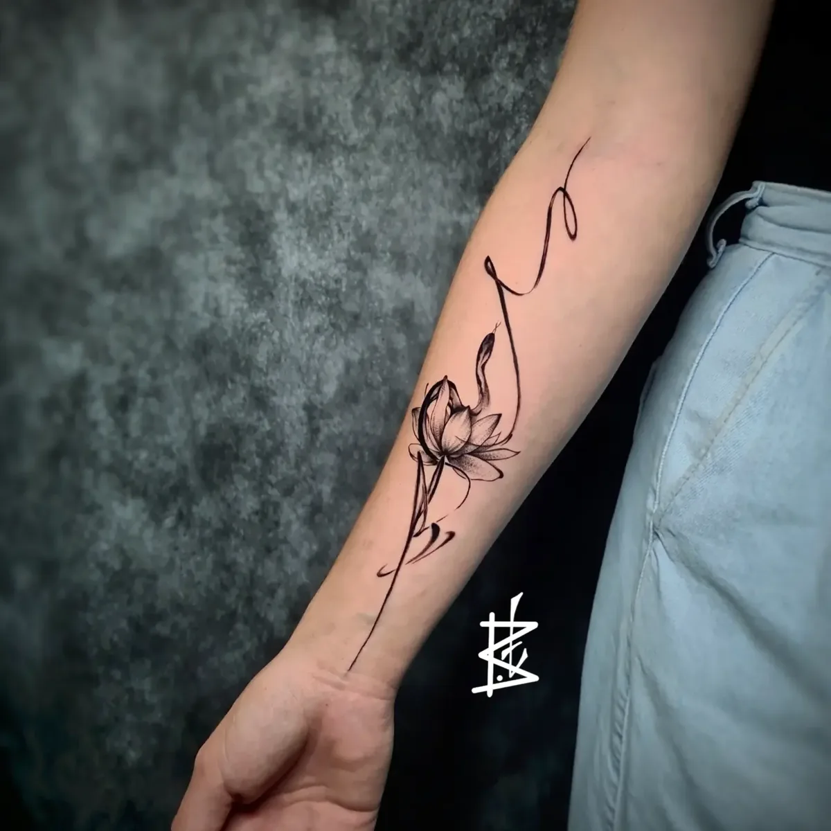 A delicate fine-line black ink tattoo featuring a lotus flower and a snake in a sketch-like style, evoking kundalini symbolism.