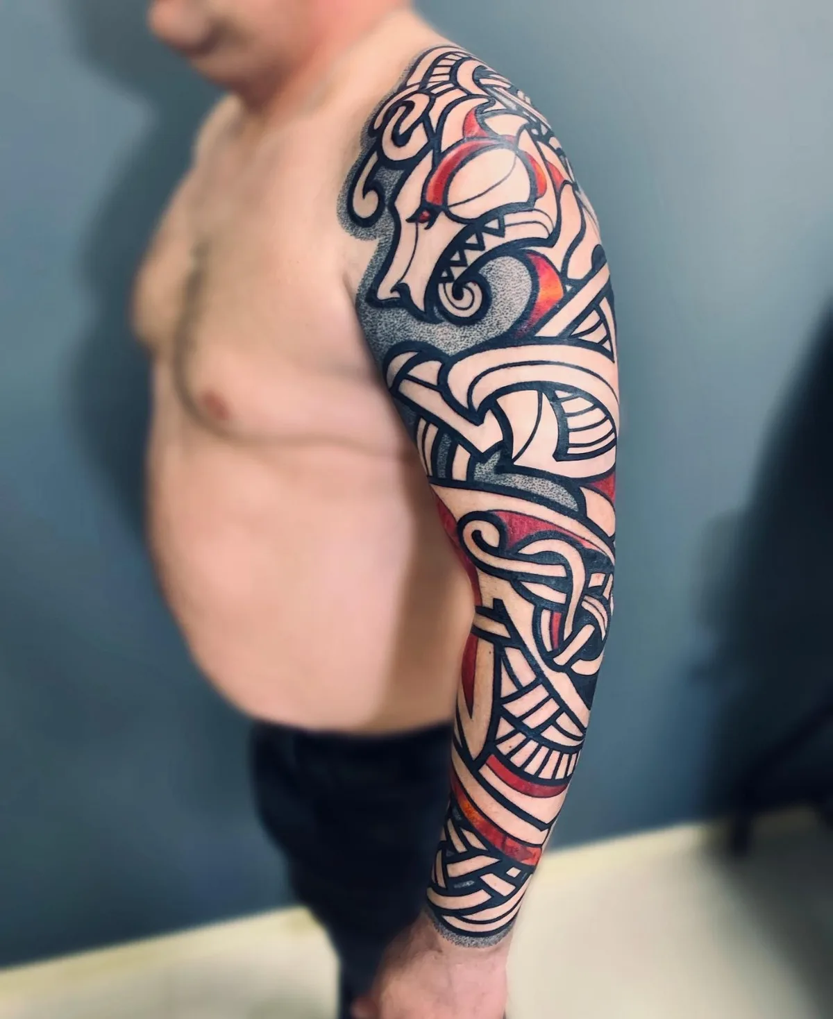 Tatouage avec entrelacs celtiques et imagerie animale stylisée, lignes noires épaisses avec accents rouges.