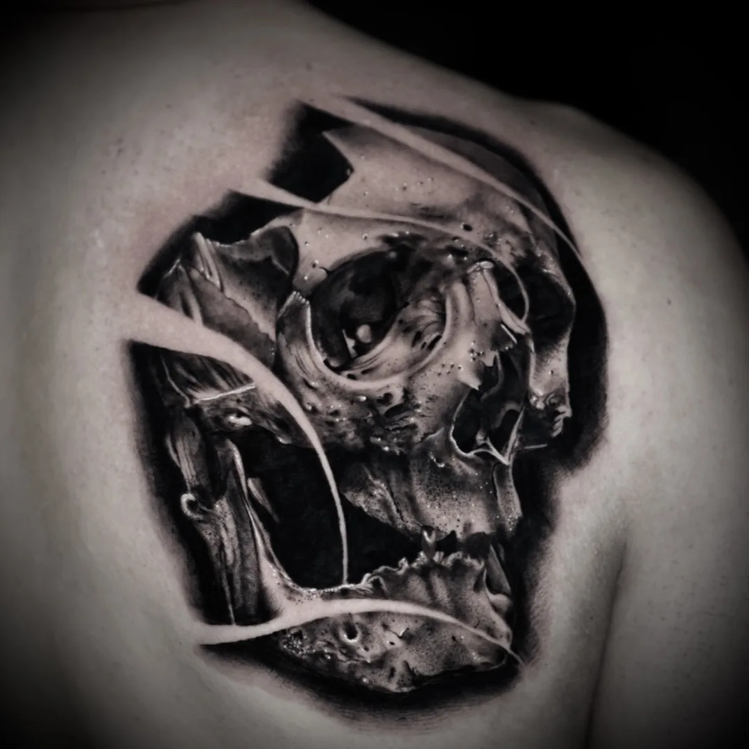 A detailed black and grey tattoo of a skull with a ripped-skin effect, highly realistic with intricate shading and detail.