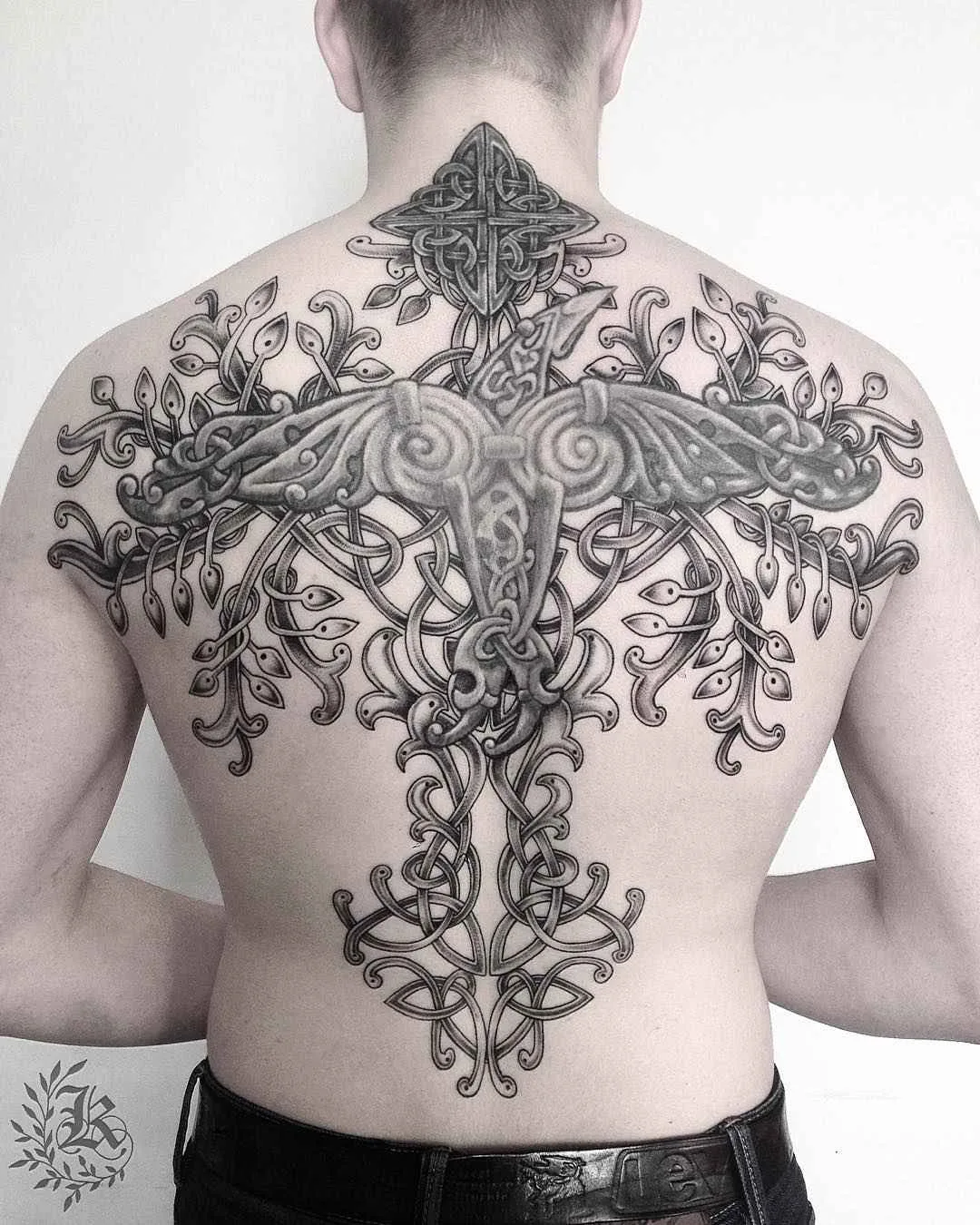 Ein großes, schwarz-graues Tattoo auf dem oberen Rücken mit einem stilisierten Vogel und Kreuz, eingebettet in keltisches Flechtwerk.