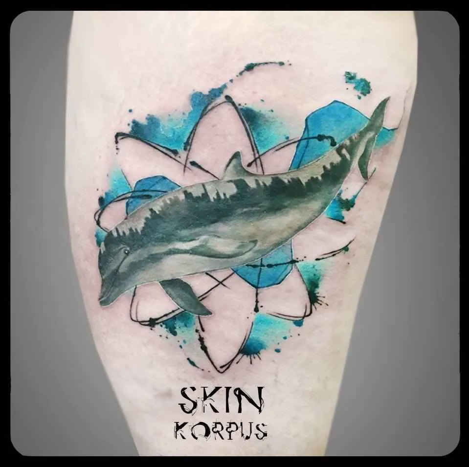 A tattoo featuring a realistically rendered dolphin set against a geometric background with splashes of blue and black watercolour.