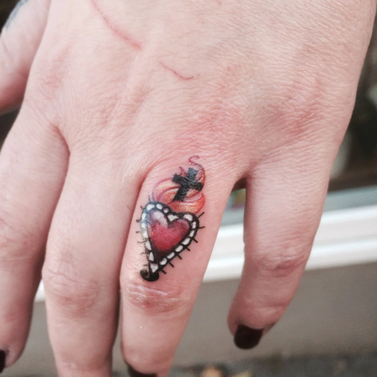 Тату в традиционном стиле: сердце с крестом и языками пламени на пальце.