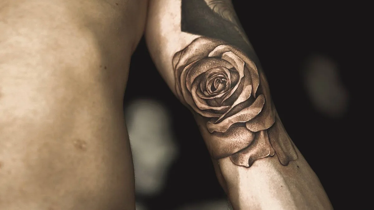 Ein detailliertes Schwarz-Grau-Tattoo einer realistischen Rose auf dem Unterarm mit feinen Schattierungen und Tiefe.