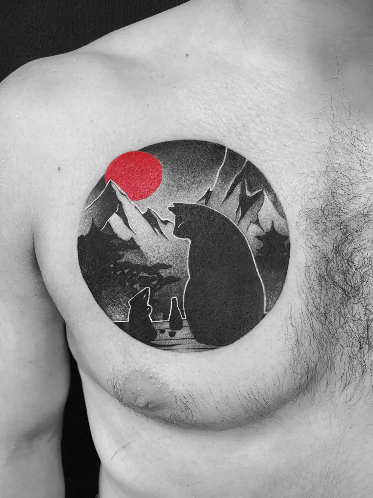 A blackwork tattoo of a bear and mountains under a red sun enclosed in a circular frame.
