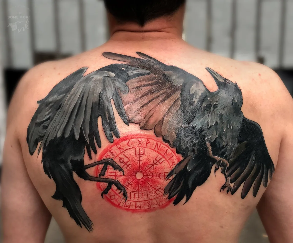 A tattoo featuring two crows with outstretched wings set against a bold red circular background decorated with Celtic knotwork symbols.