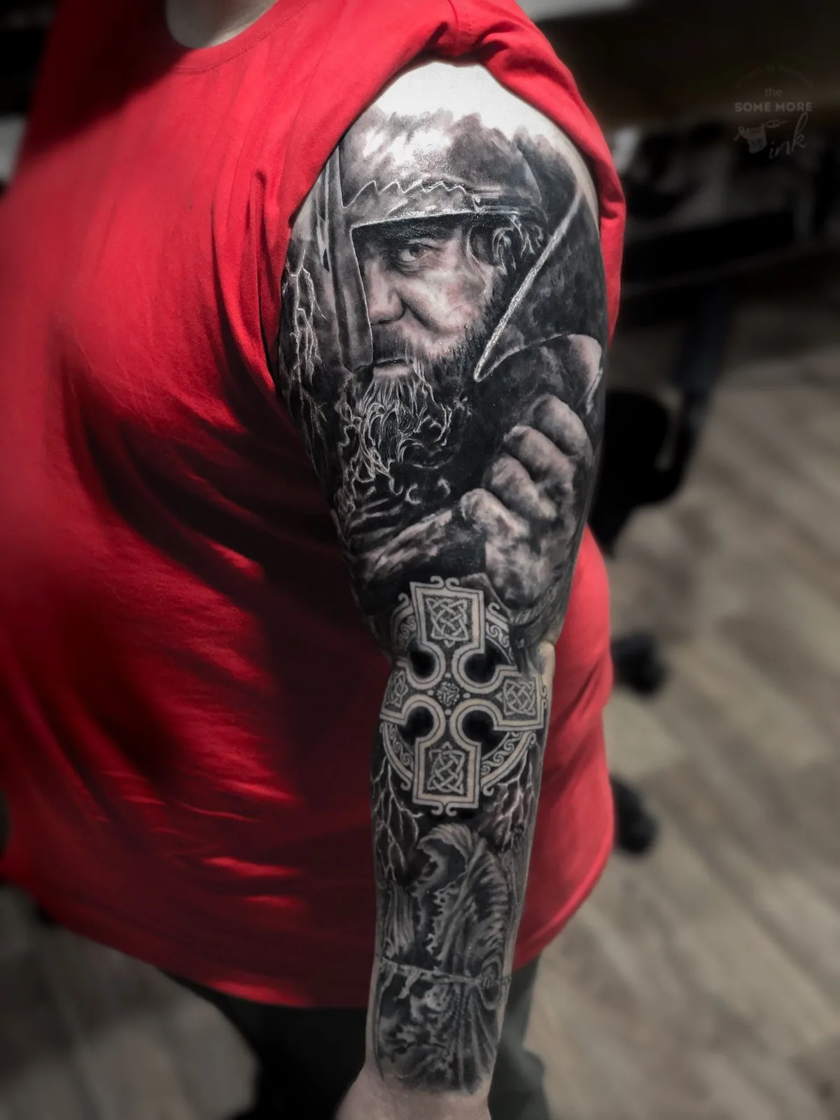 Ein detailliertes schwarz-graues Full-Sleeve-Tattoo mit einem Krieger-Portrait, einem keltischen Kreuz und weiteren illustrativen Elementen.