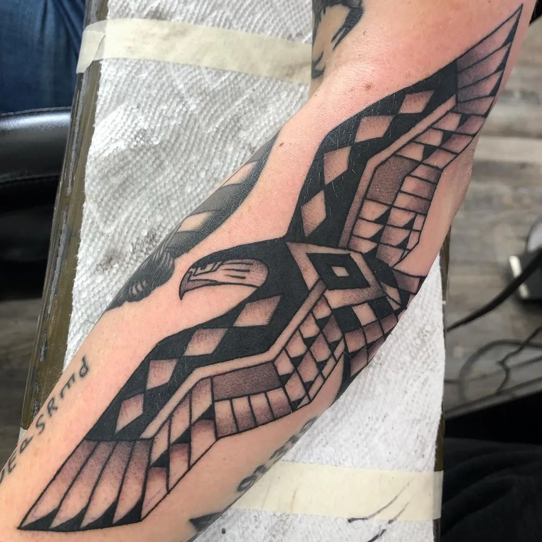 Geometric eagle tattoo with black and grey shading, the bird's form divided into angular tribal-influenced shapes.