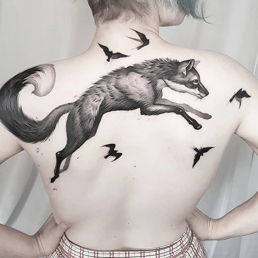 A black and grey tattoo of a running fox accompanied by several birds in flight, rendered in a realistic illustrative style.