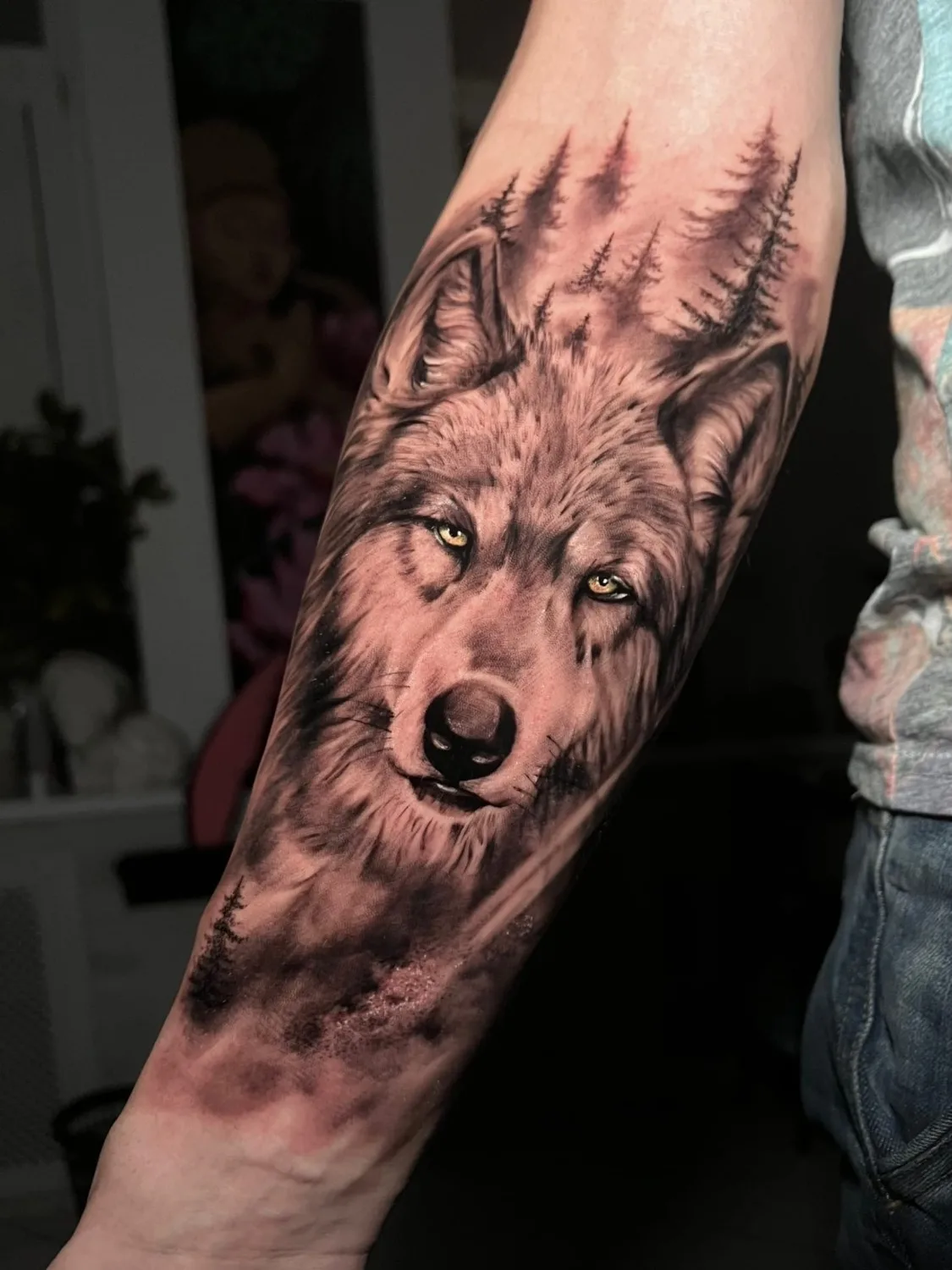 A detailed black and grey tattoo of a wolf's face with a forest scene in the background.