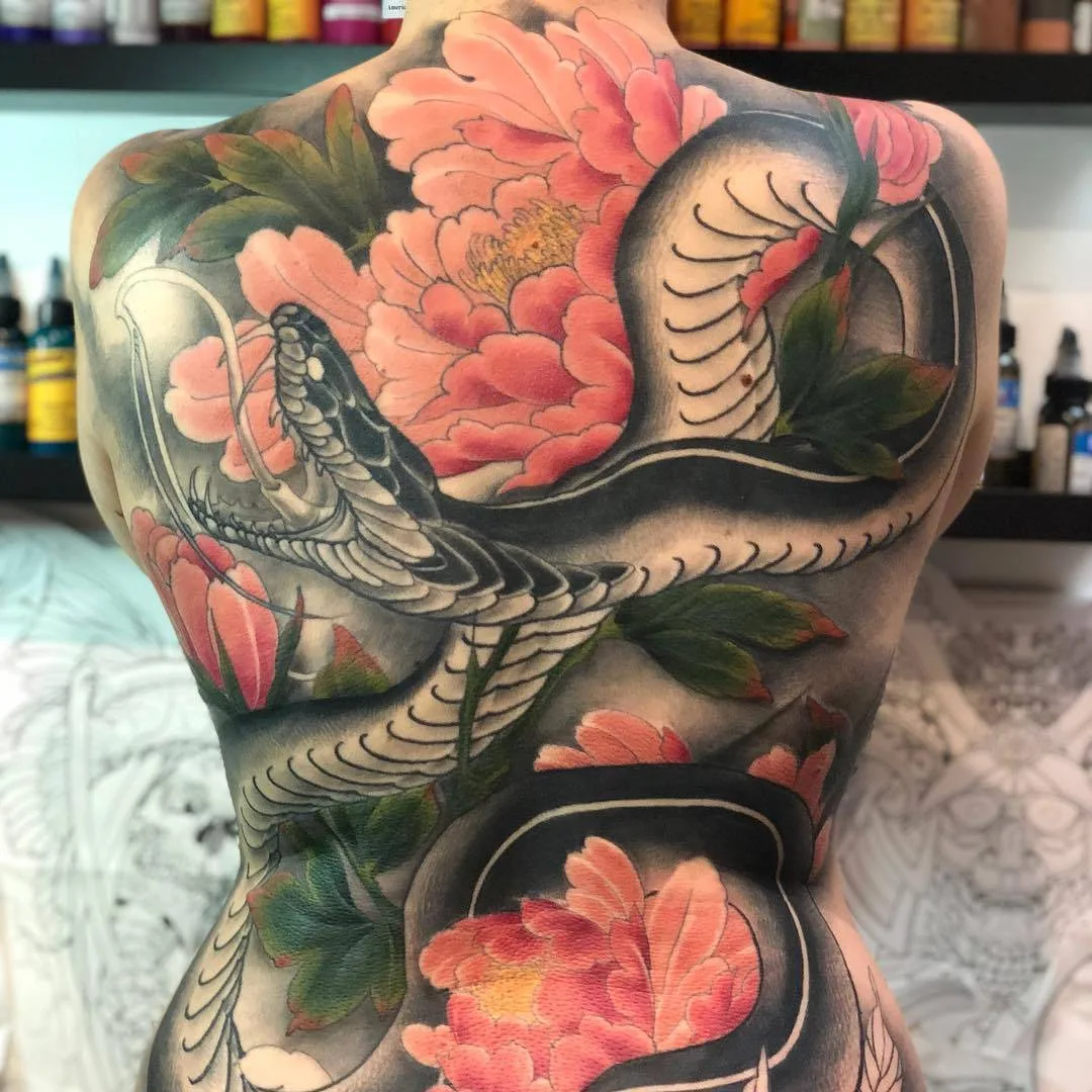A large colourful Japanese-style tattoo covering the entire back, featuring a snake intertwined with flowers in a flowing, scene-based composition.