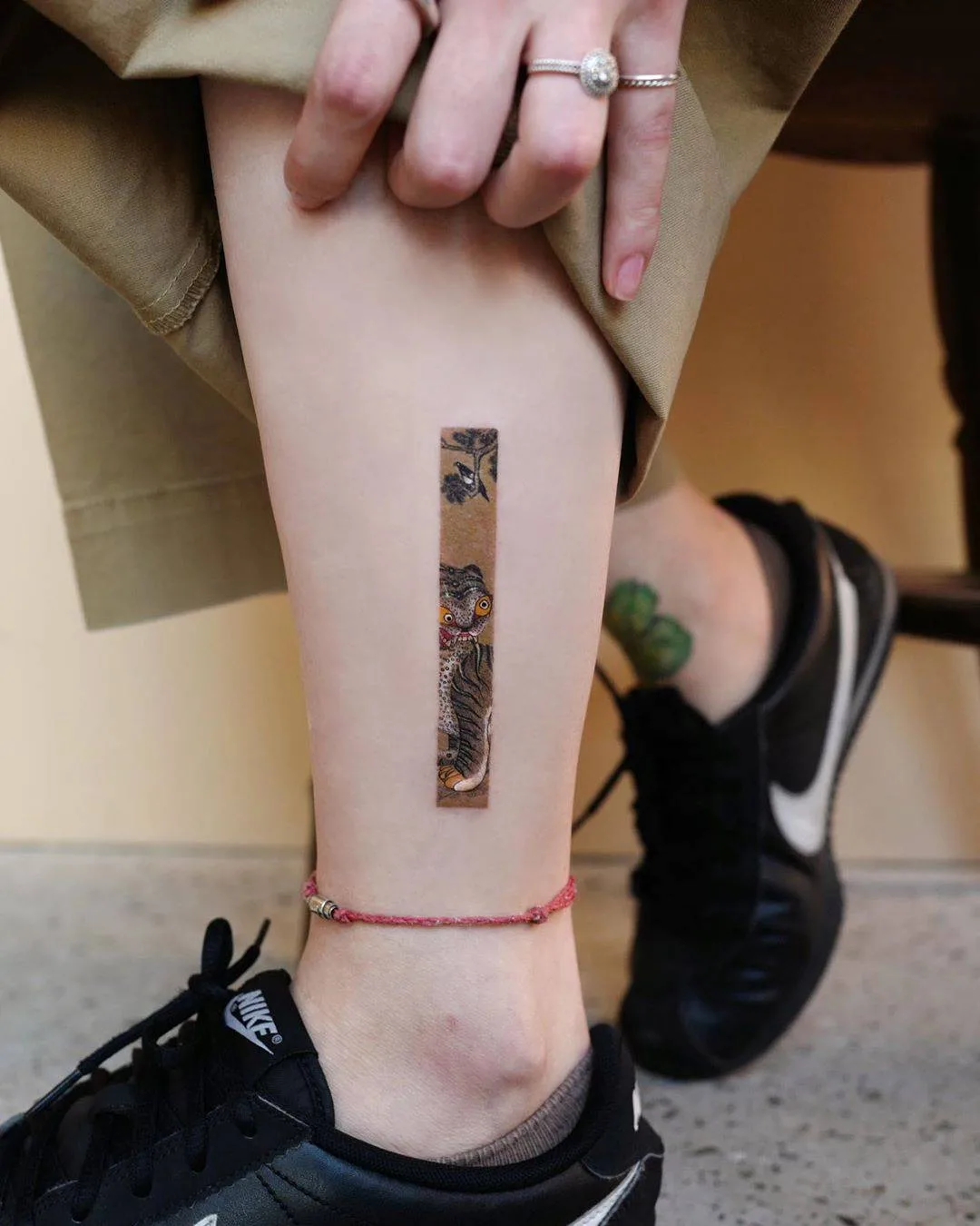 A small rectangular tattoo featuring a stylized tiger and floral elements in a Japanese-inspired style.