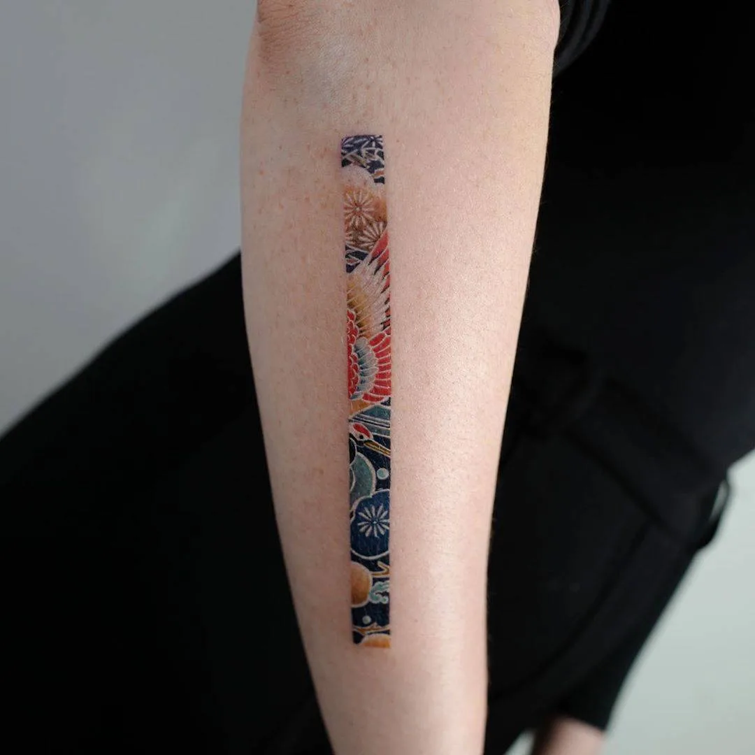 A vertical strip tattoo featuring a crane in flight surrounded by floral patterns in a colorful Japanese-inspired style.