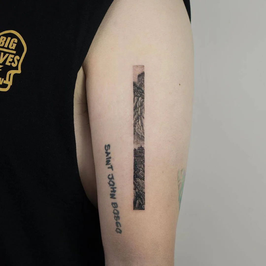 A black and grey fineline tattoo of a landscape scene with the words 'Saint John Bosco' written below it.