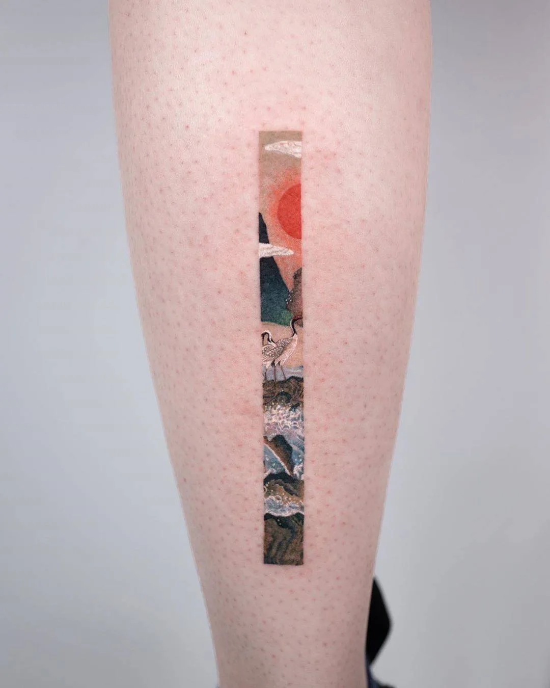 A rectangular watercolor-style tattoo depicting a Japanese landscape with birds, a sun, and mountains.
