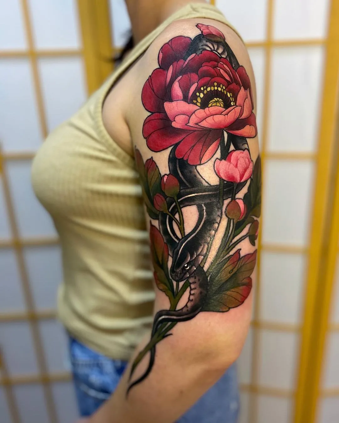 A vibrant neo-traditional tattoo featuring a snake intertwined with a large peony flower and foliage, with rich colour and detailed linework.