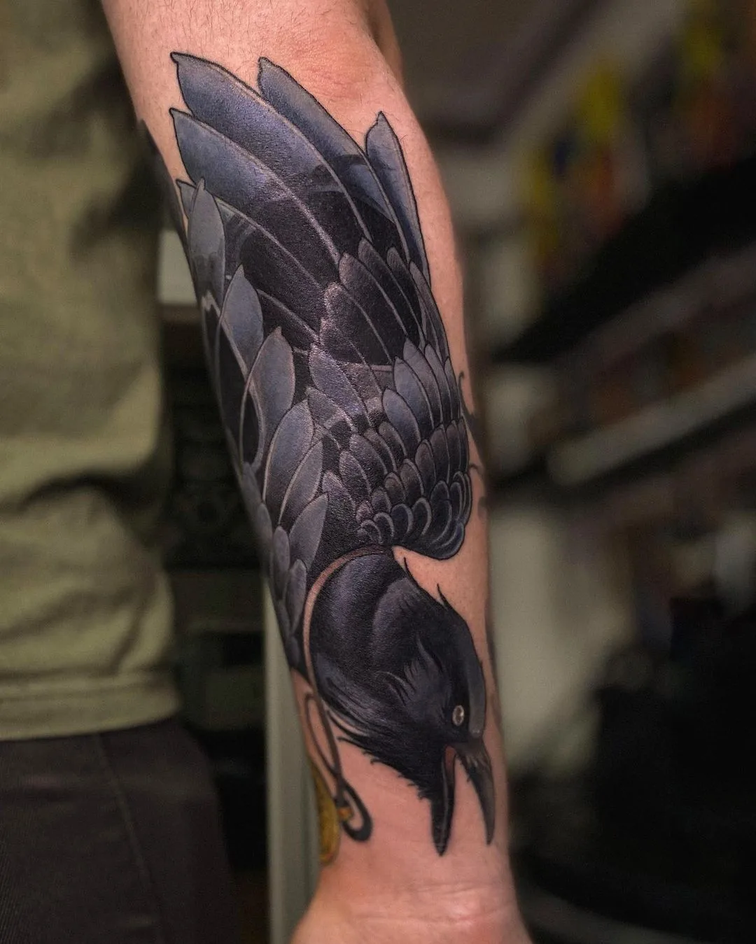 A detailed black and grey realistic tattoo of a crow with its wings fully spread, showing intricate feather shading and structure.