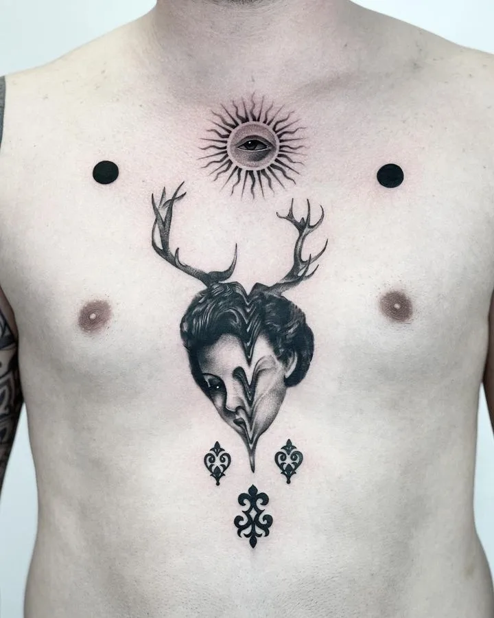 A surreal blackwork tattoo featuring a melting face with deer antlers, an eye within a sun motif, and ornamental designs.
