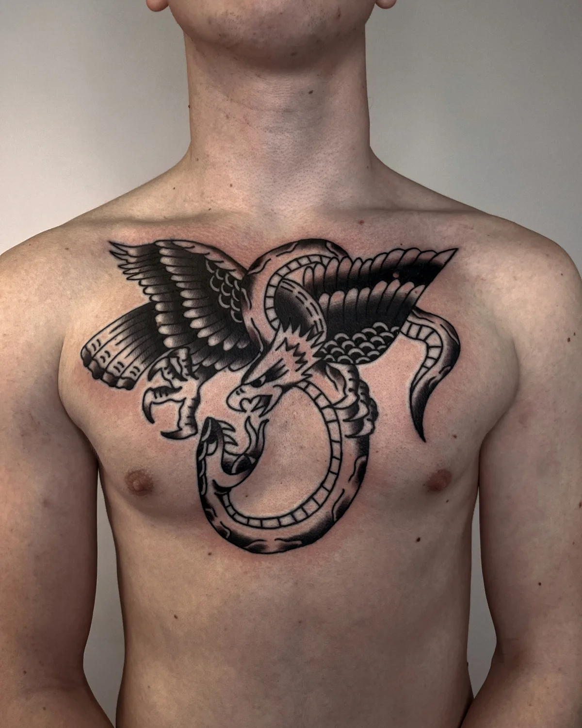 Tatouage de style traditionnel représentant un aigle et un serpent entrelacés, réalisé en encre noire pleine.