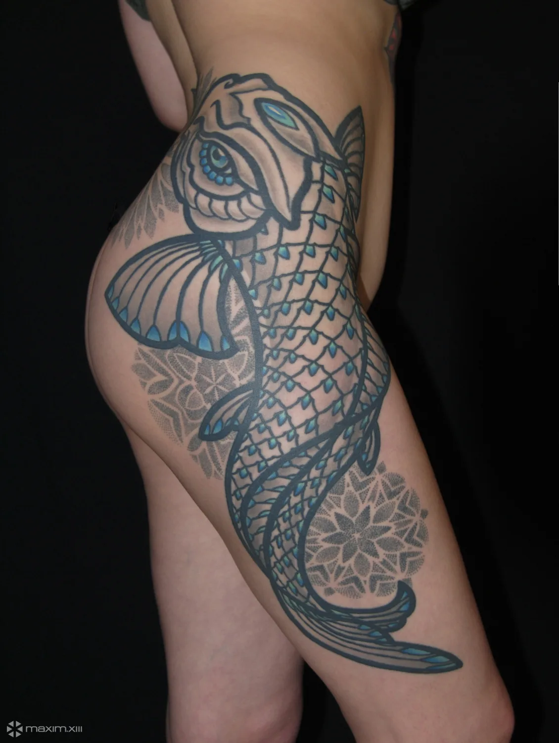 A large tattoo on the thigh featuring a koi fish rendered in geometric style with dotwork mandala elements and blue accent colour.