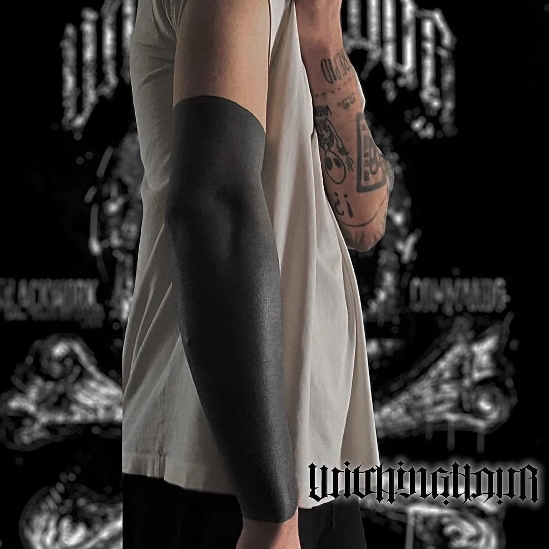 A full sleeve tattoo completely filled in with black ink. The style is a bold blackout.