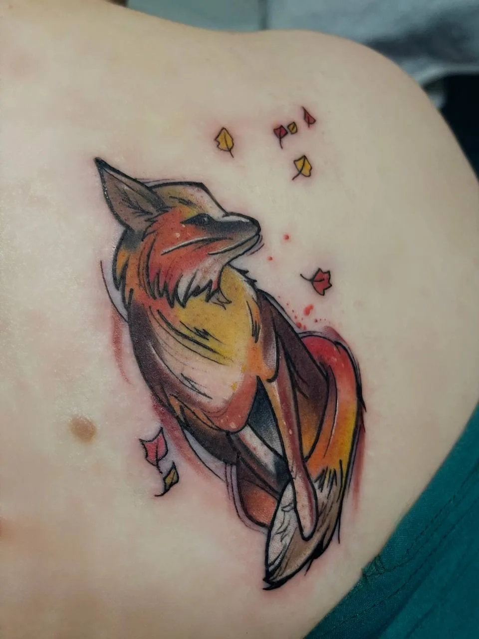 A watercolor-style tattoo of a fox with falling autumn leaves, rendered in warm orange and red tones.