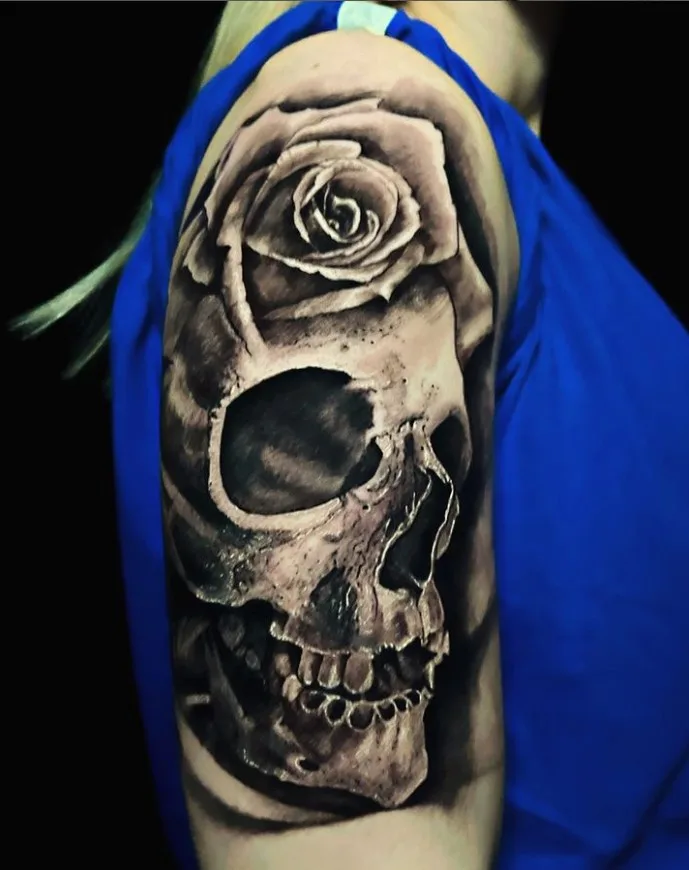A realistic black and grey tattoo of a skull with a rose placed on top of it.