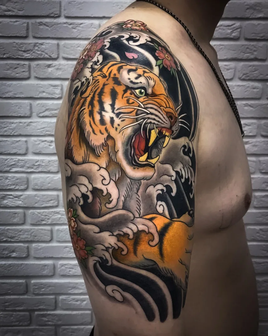 A vibrant Japanese-style tattoo on the arm featuring a roaring tiger amid crashing waves and cherry blossom branches.