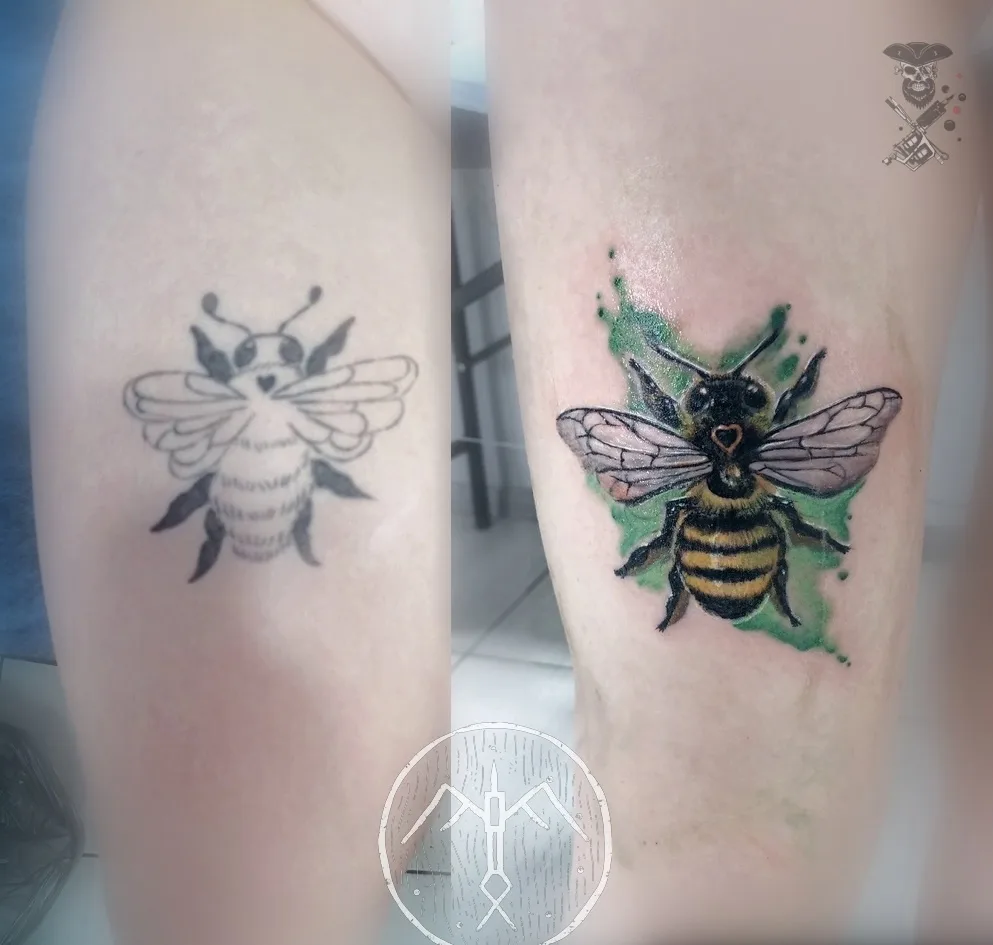A realistic bee tattoo with watercolor-style green accents placed over an older, simpler bee design, demonstrating how a new piece can transform a previous tattoo.