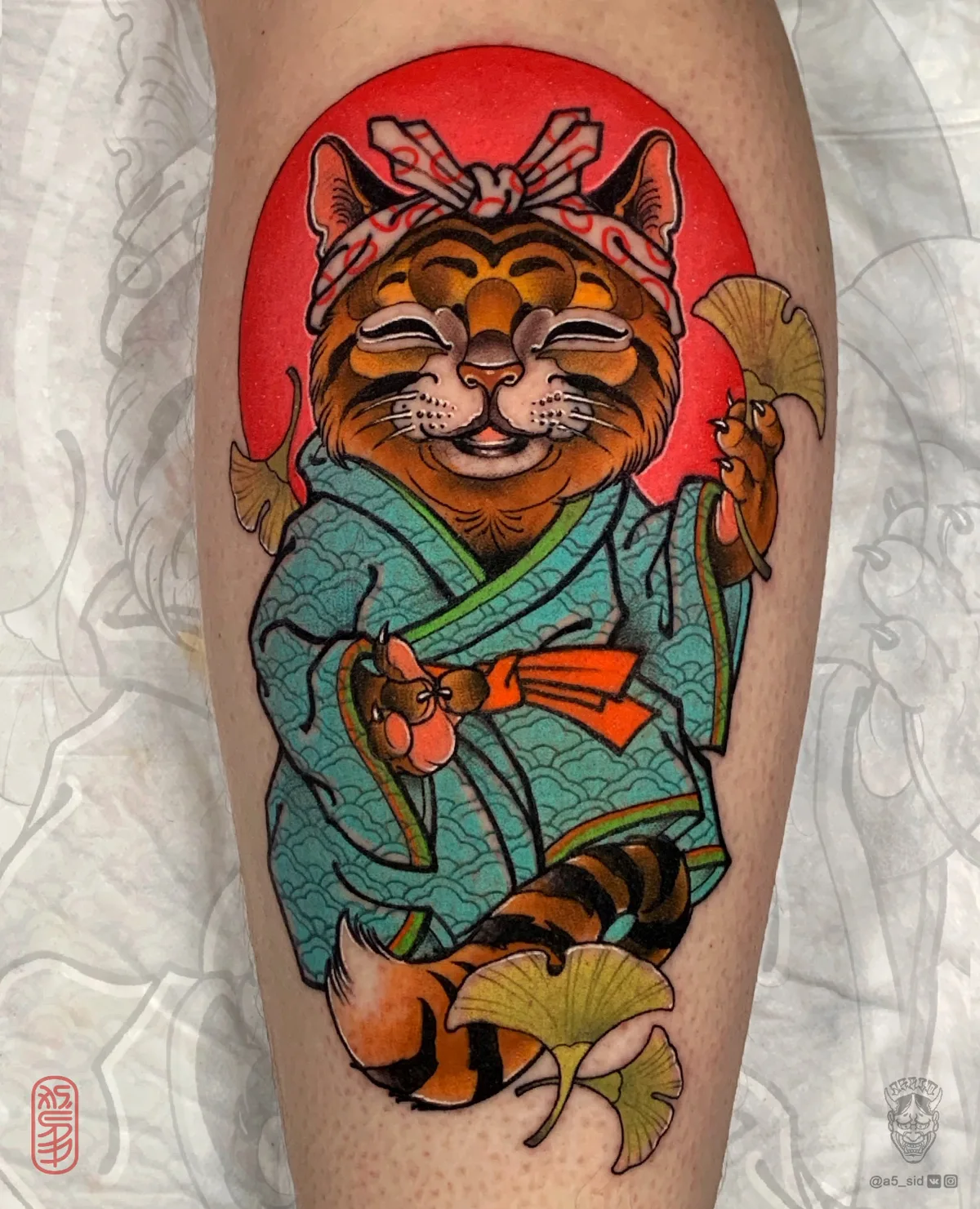 A colorful neo-traditional tattoo of a smiling beckoning cat dressed in traditional Japanese clothing and holding ginkgo leaves, rendered in vivid saturated tones.