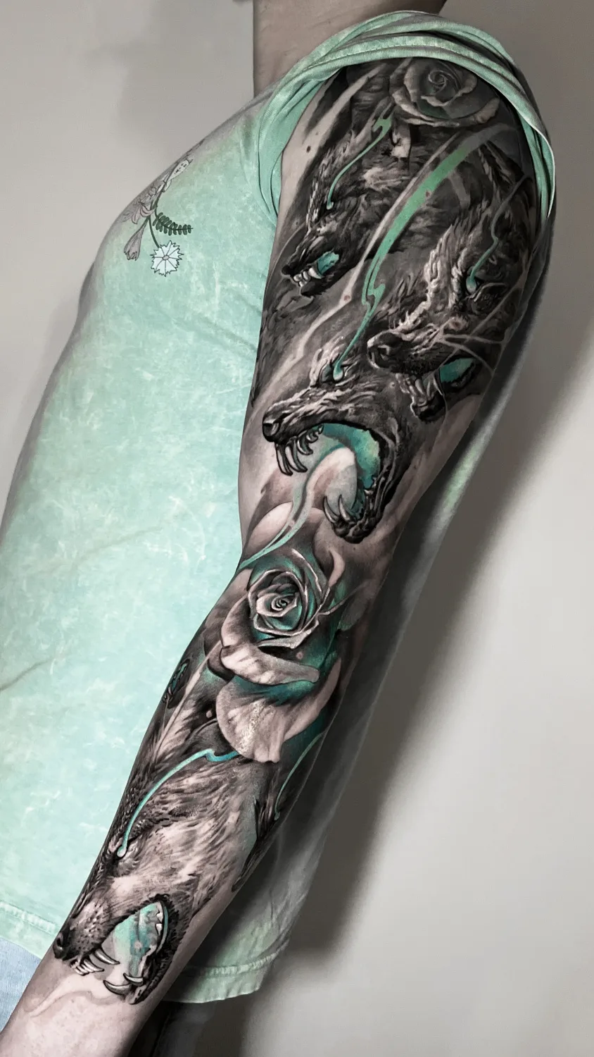 A detailed black and grey tattoo featuring wolves and roses with teal accents, covering the entire arm.