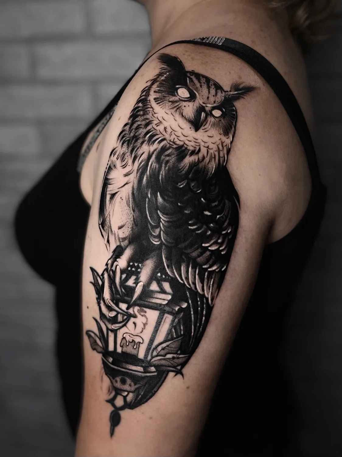 A detailed blackwork tattoo of an owl perched on a lantern, featuring intricate shading and linework in solid black ink.