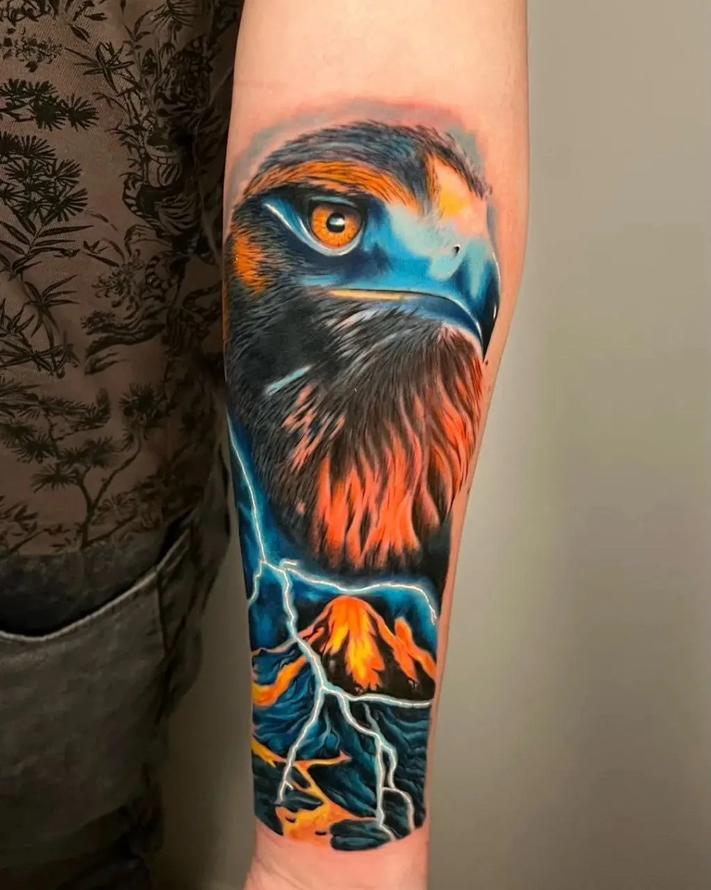 Realistic tattoo of an eagle's head with a mountain range and lightning bolt in the background.