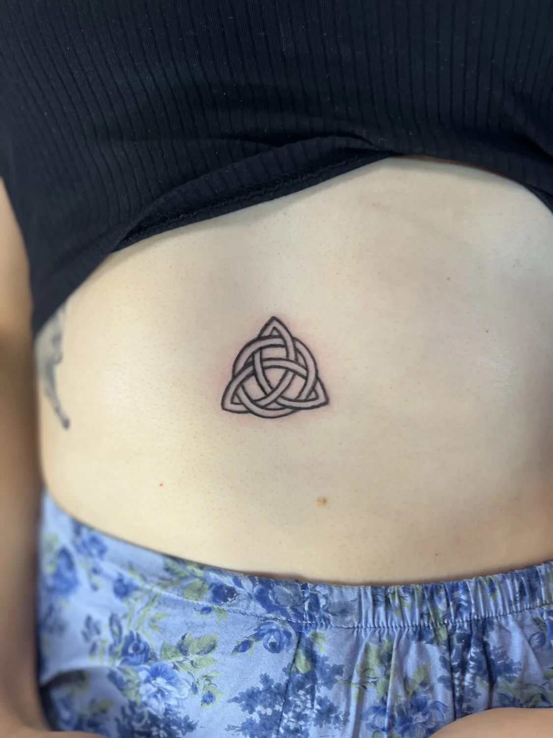 Ein kleines, geometrisches keltisches Knotenmuster als Tattoo auf dem Bauch, schlicht und präzise ausgeführt.