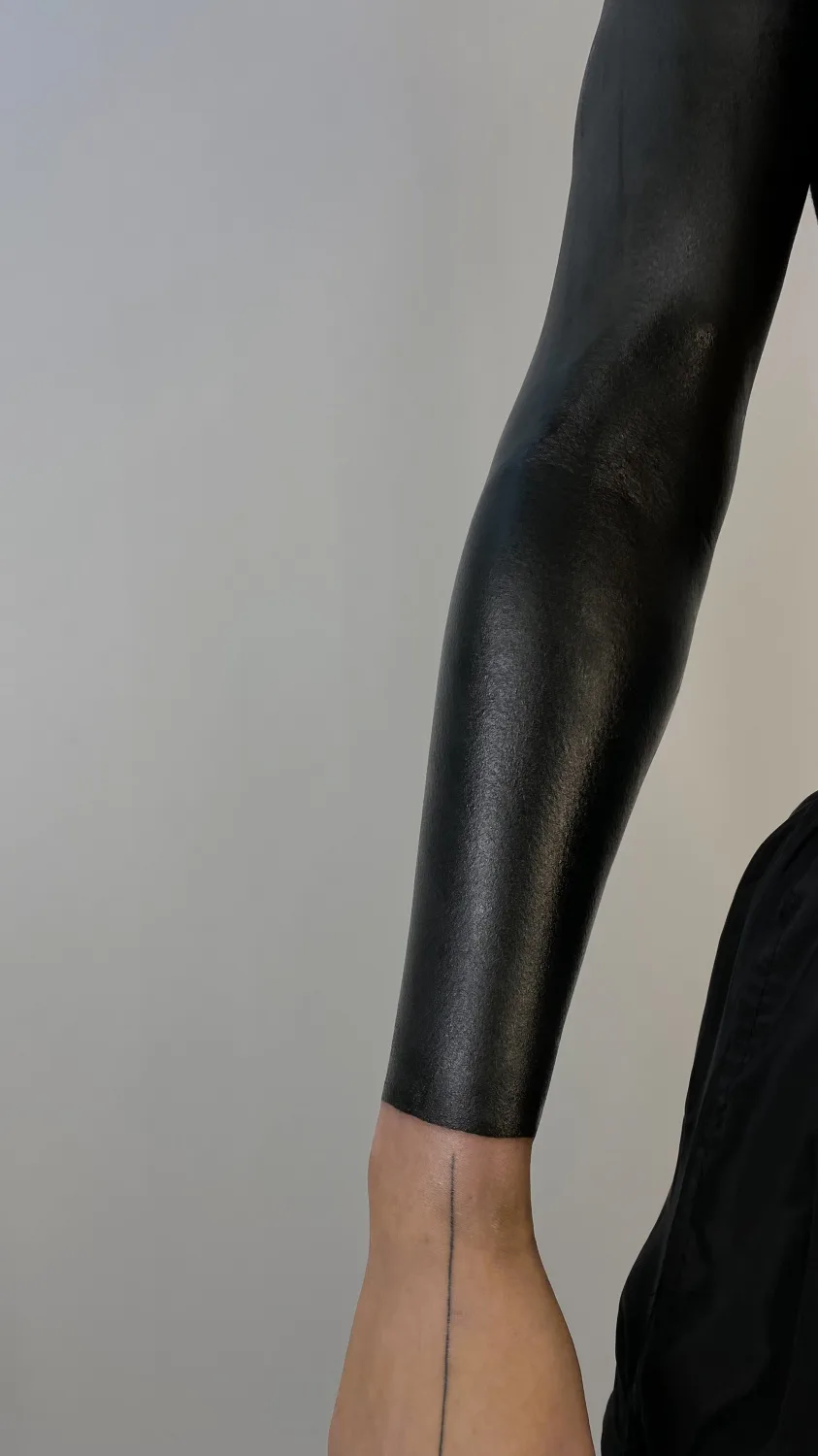 A full blackout tattoo covering the forearm. A single line is visible on the wrist.
