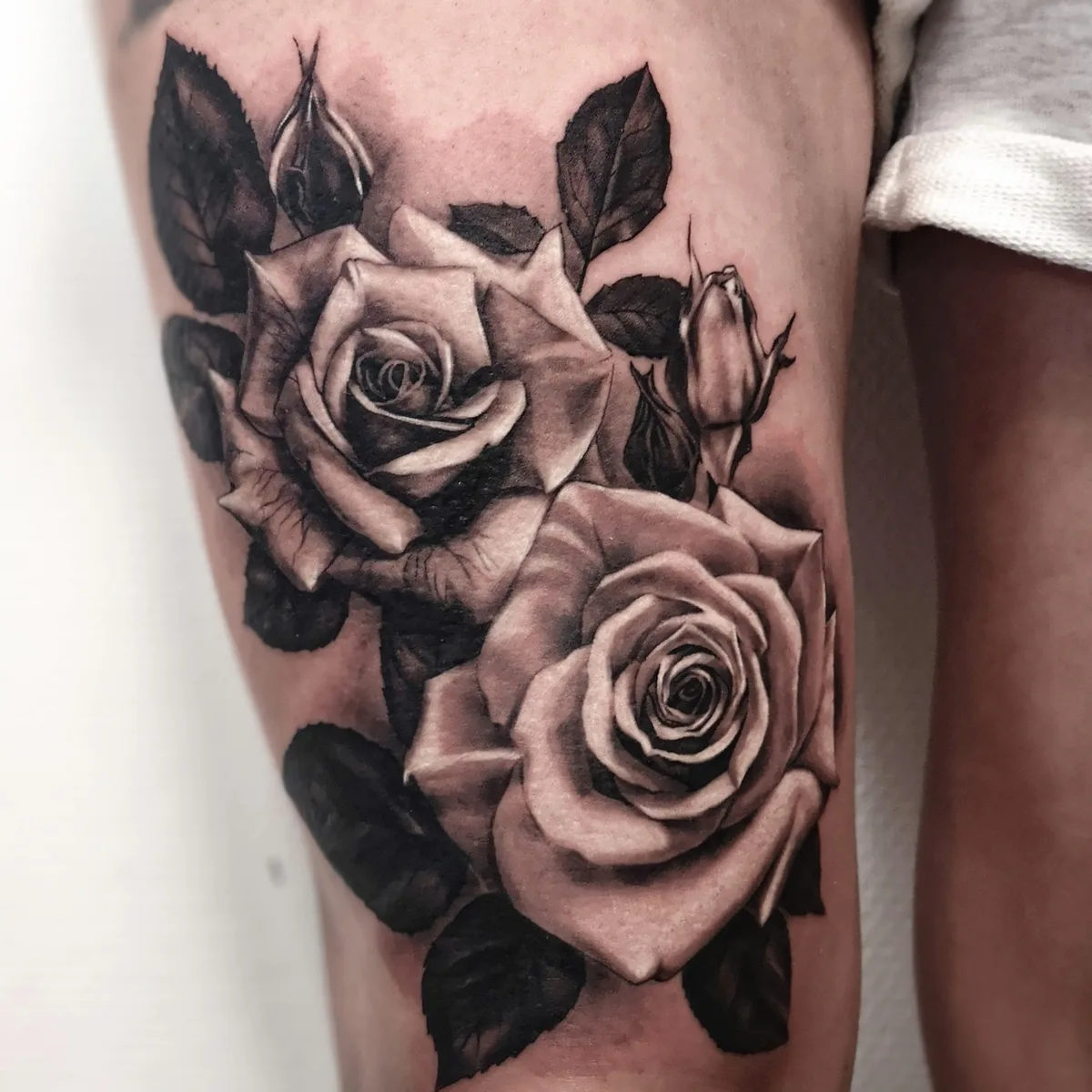 Ein detailliertes Schwarz-Grau-Tattoo von zwei Rosen mit Blättern und Knospen in verschiedenen Blühstadien.