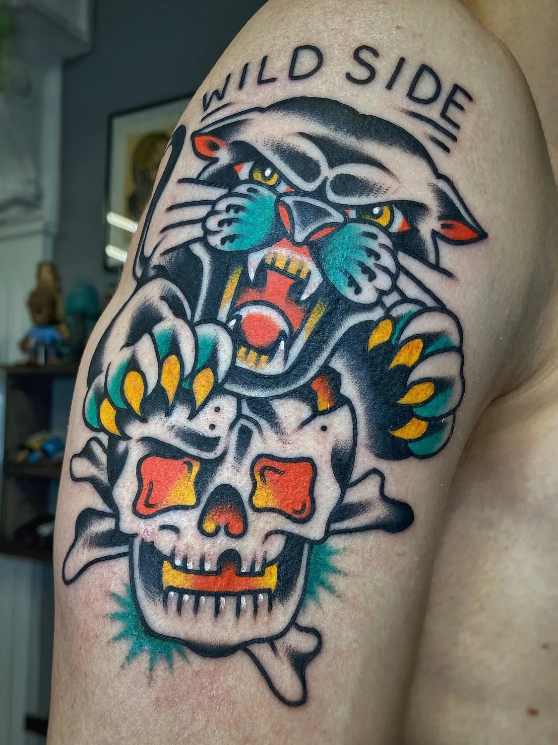 A traditional style tattoo featuring a panther, skull with crossbones, and the words 'WILD SIDE' in bold lettering.