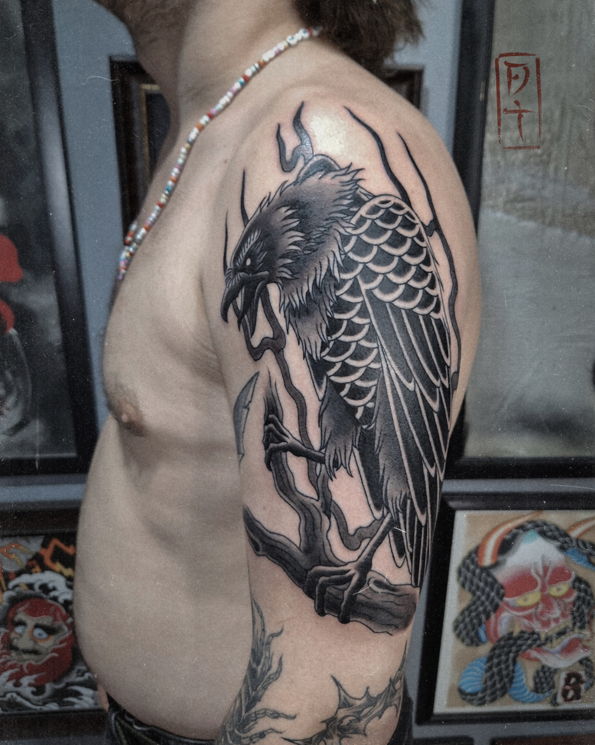 A detailed blackwork tattoo of a raven perched on a branch, incorporating Japanese aesthetic influences in the composition and brushwork-style linework.