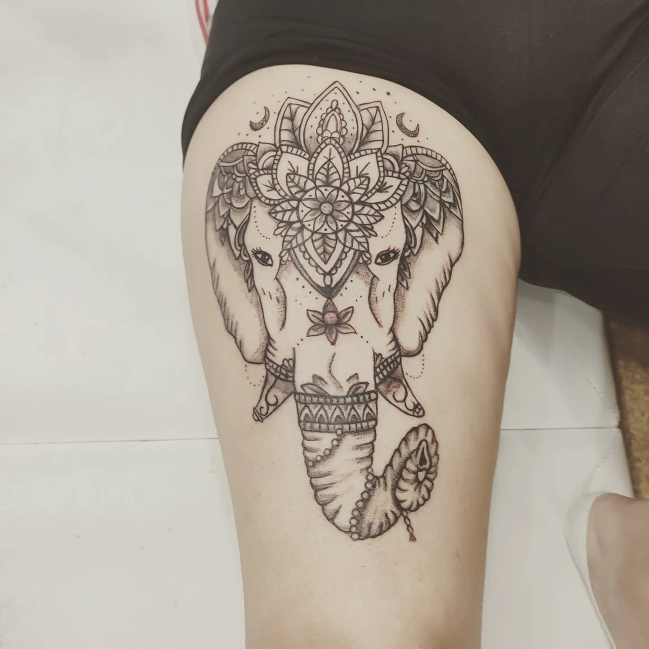 A bold blackwork tattoo of an elephant wearing an ornate mandala-style headdress decorated with floral accents, combining geometric and organic motifs.