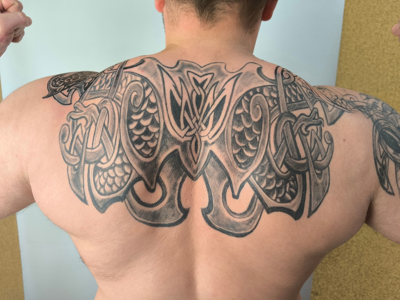 Ein großes schwarz-graues Tattoo auf dem oberen Rücken mit keltischem Flechtmuster und Drachenmotiven.