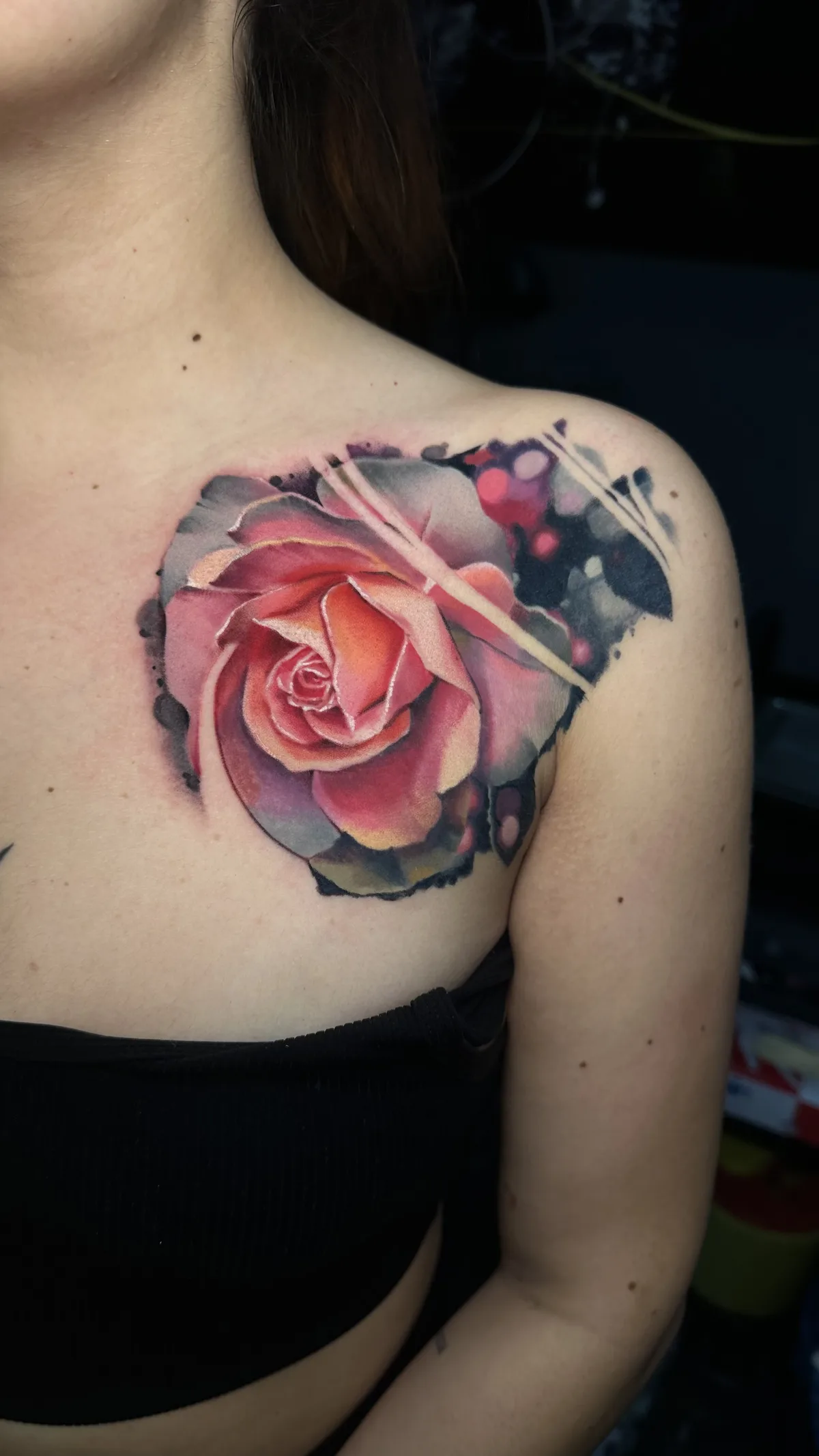 Aquarell-Rosen-Tattoo in sanften Pastelltönen auf der Schulter, vor einem dunklen, abstrakten Hintergrund, der Tiefe und Kontrast andeutet.