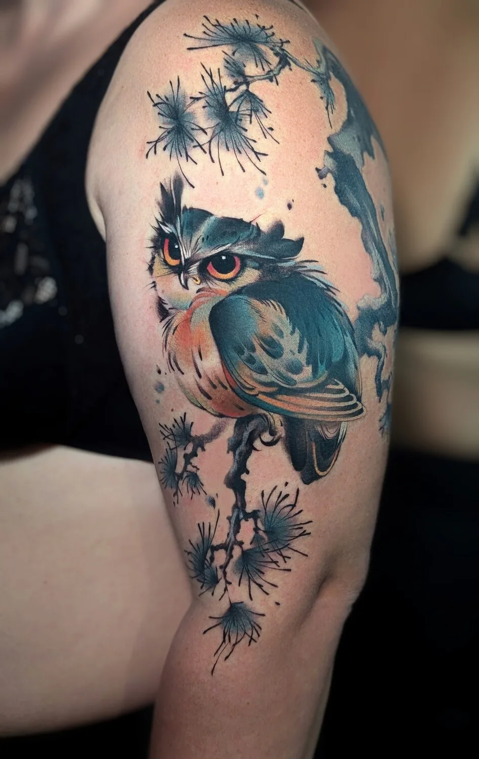 A colorful owl tattoo perched on a branch with a Japanese-inspired aesthetic, featuring warm tones and decorative linework.