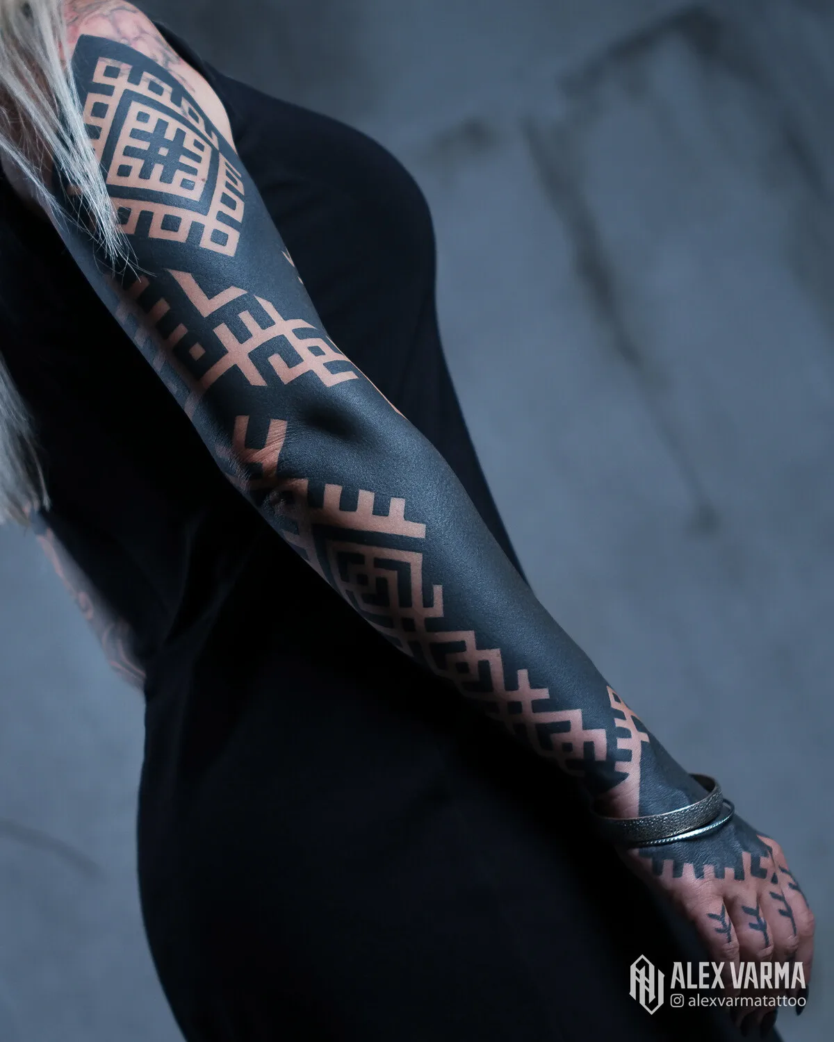 A full sleeve tattoo featuring bold black geometric patterns and blackout elements.