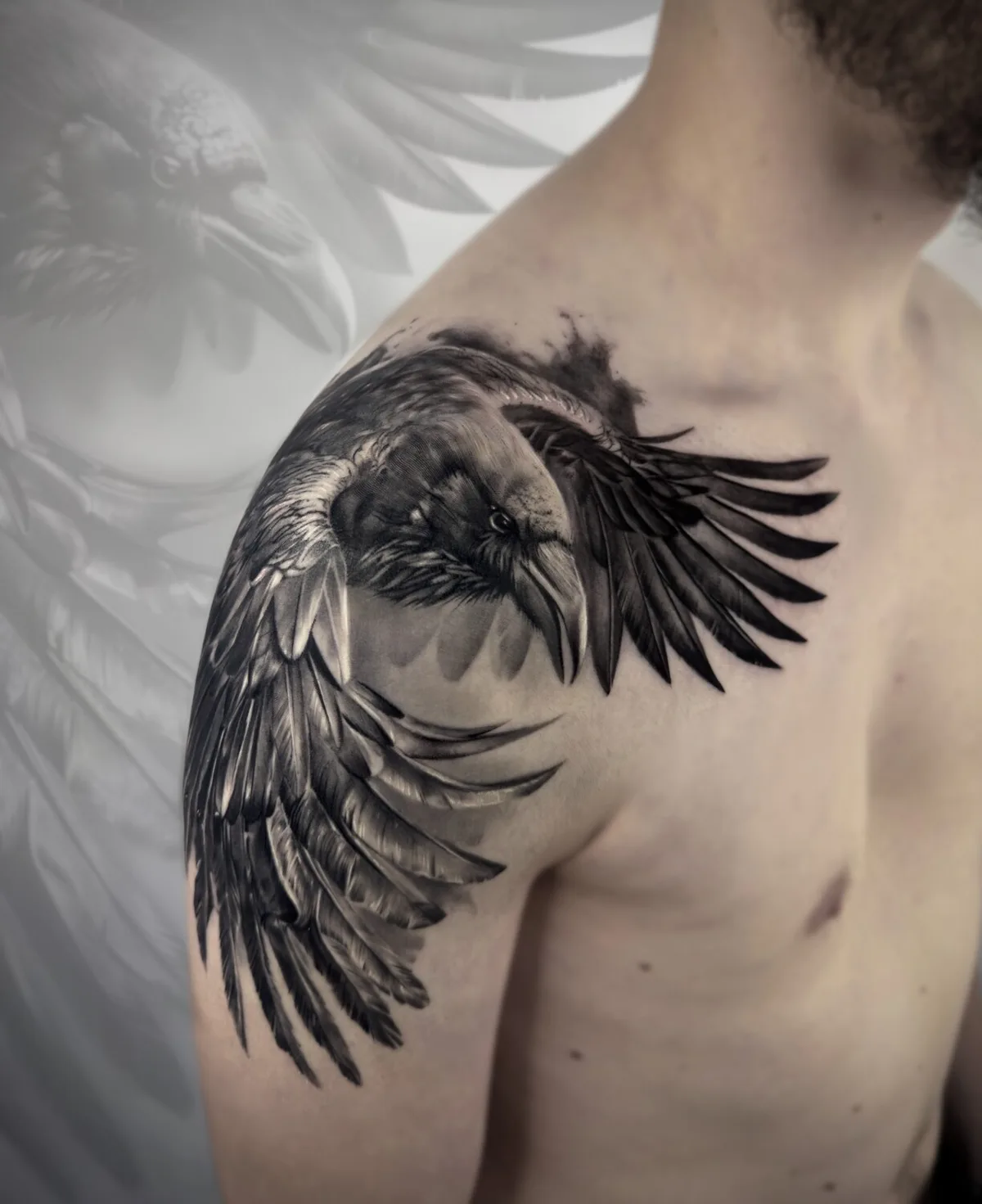 A black and grey tattoo of a raven with its wings fully spread, positioned across the shoulder blade, with detailed feather rendering and strong contrast.