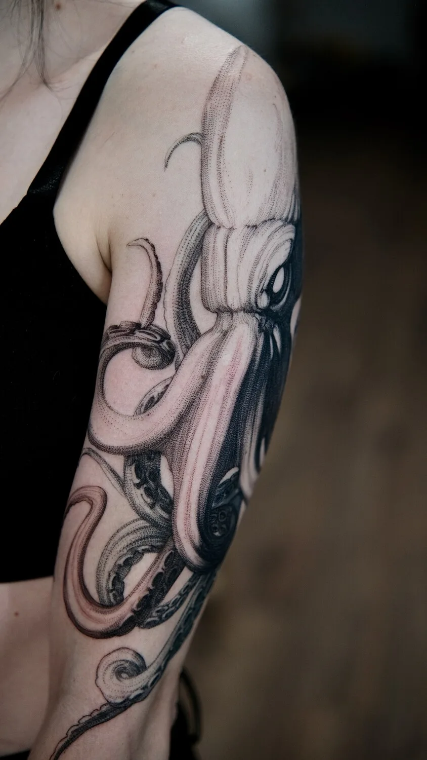A black and grey octopus tattoo rendered in a detailed engraving style, covering the full arm with fine linework and cross-hatching.