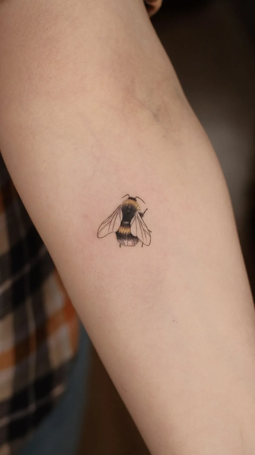 A small bee tattoo with realistic shading and fine linework, showing the insect's body segments, wings, and legs rendered with careful detail at a compact scale.