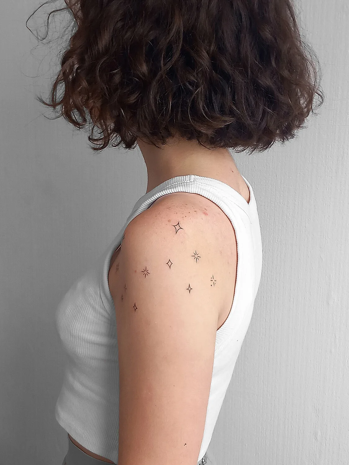 A minimalist tattoo of small star shapes placed on the shoulder. The design is subtle and delicate with fine black linework.