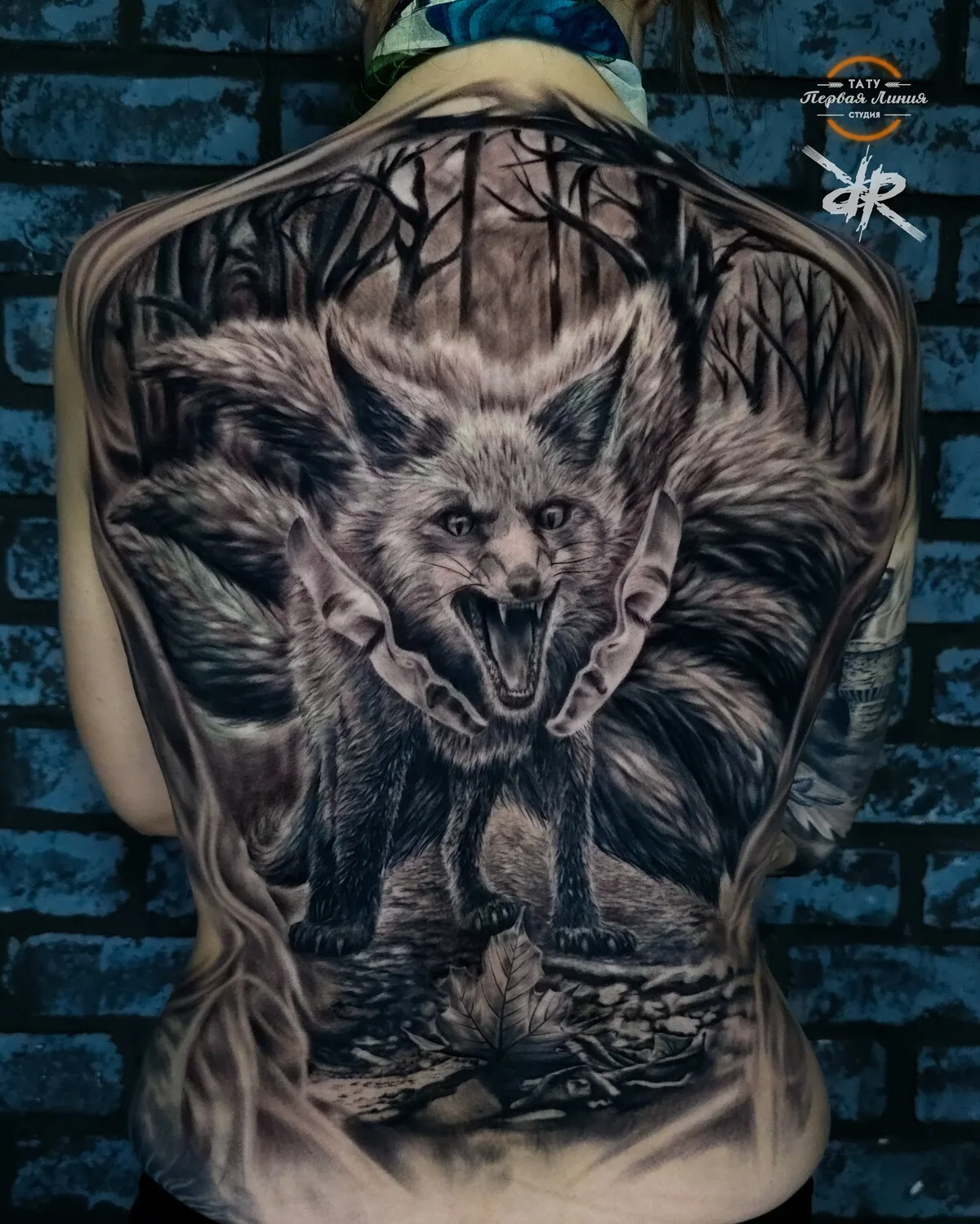 A black and grey tattoo of a snarling fox surrounded by dark forest trees, rendered in a detailed realistic style.
