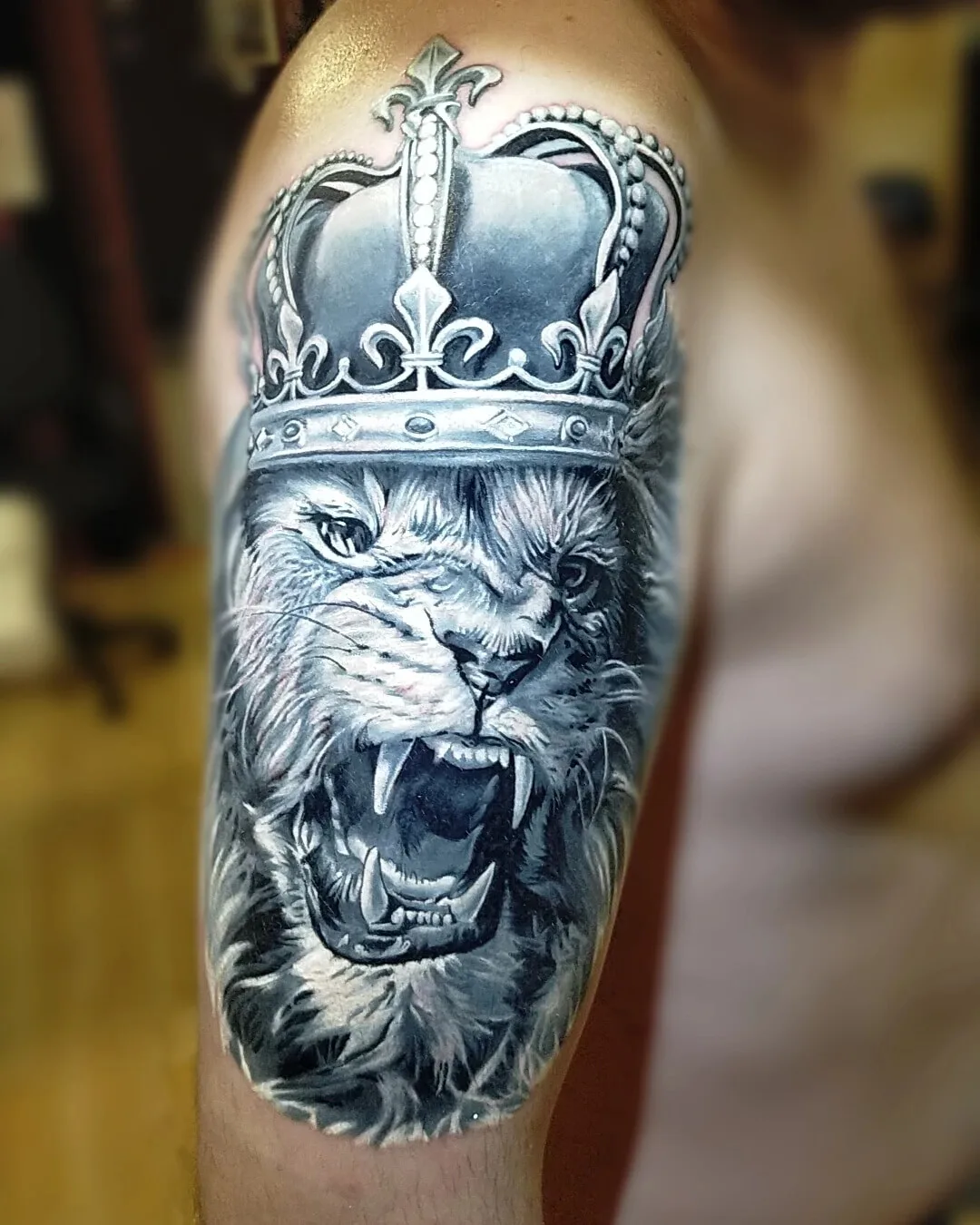 Tatuaggio realistico in bianco e nero di un leone ruggente che indossa una corona, con shading dettagliato e texture del pelo.