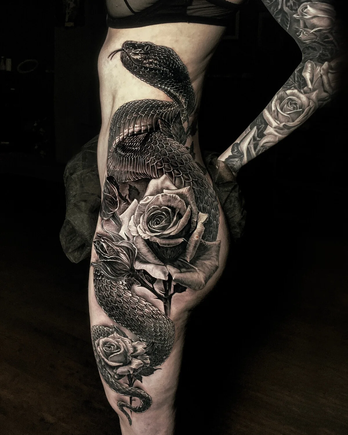Ein detailliertes Schwarz-Grau-Tattoo mit einer Schlange, die sich mit Rosen verschlingt und die Seite des Körpers bedeckt.